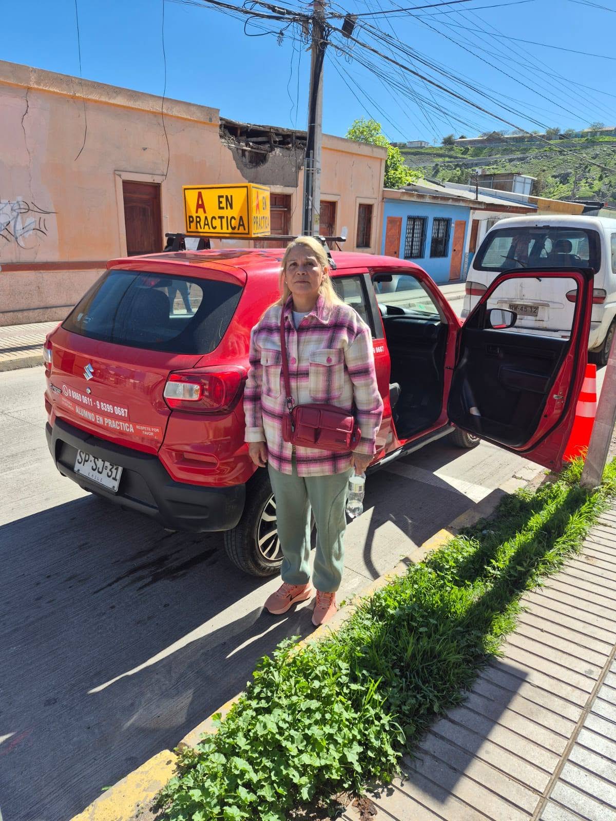 Alumna junto al auto rojo de la escuela con la puerta abierta, en Vallenar