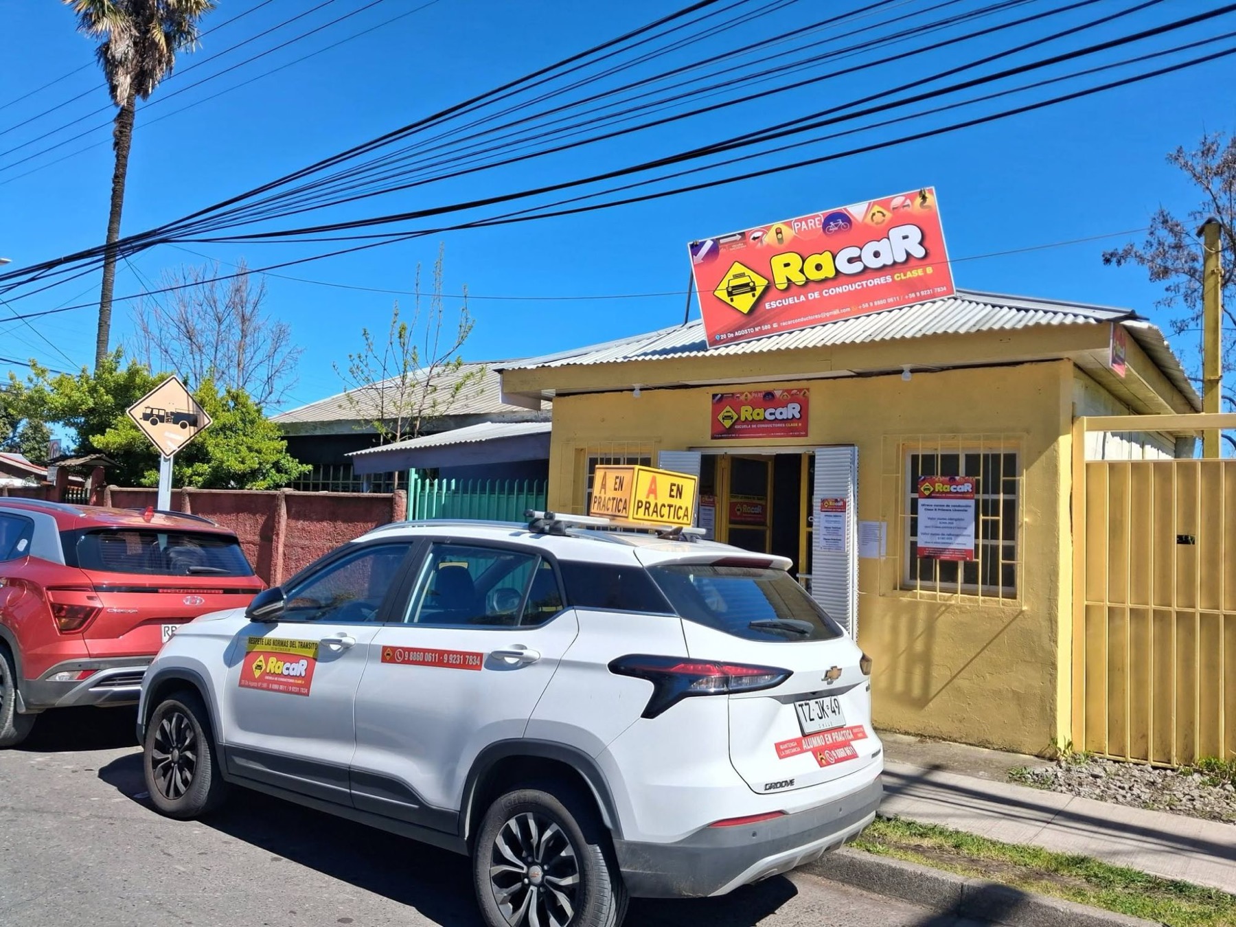 Fachada amarilla de la sucursal de Chillán Viejo con el letrero rojo de RacaR y un auto con el cartel A en práctica